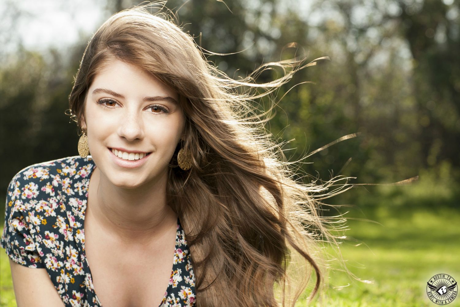 Best Austin senior portraits taken at Butler Park of high school senior girl in flowered dress with hair blowing in the wind.